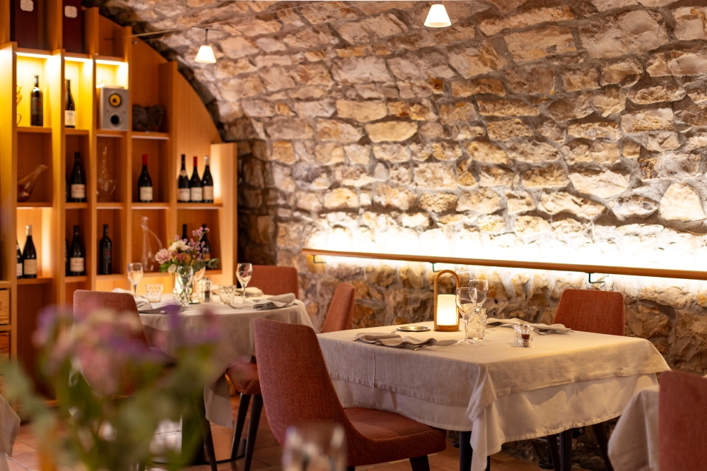 tables de restaurant dans l'ambiance cosy d'une salle voutée en vieilles pierres cévénoles et bouteilles de vin en arrière plan